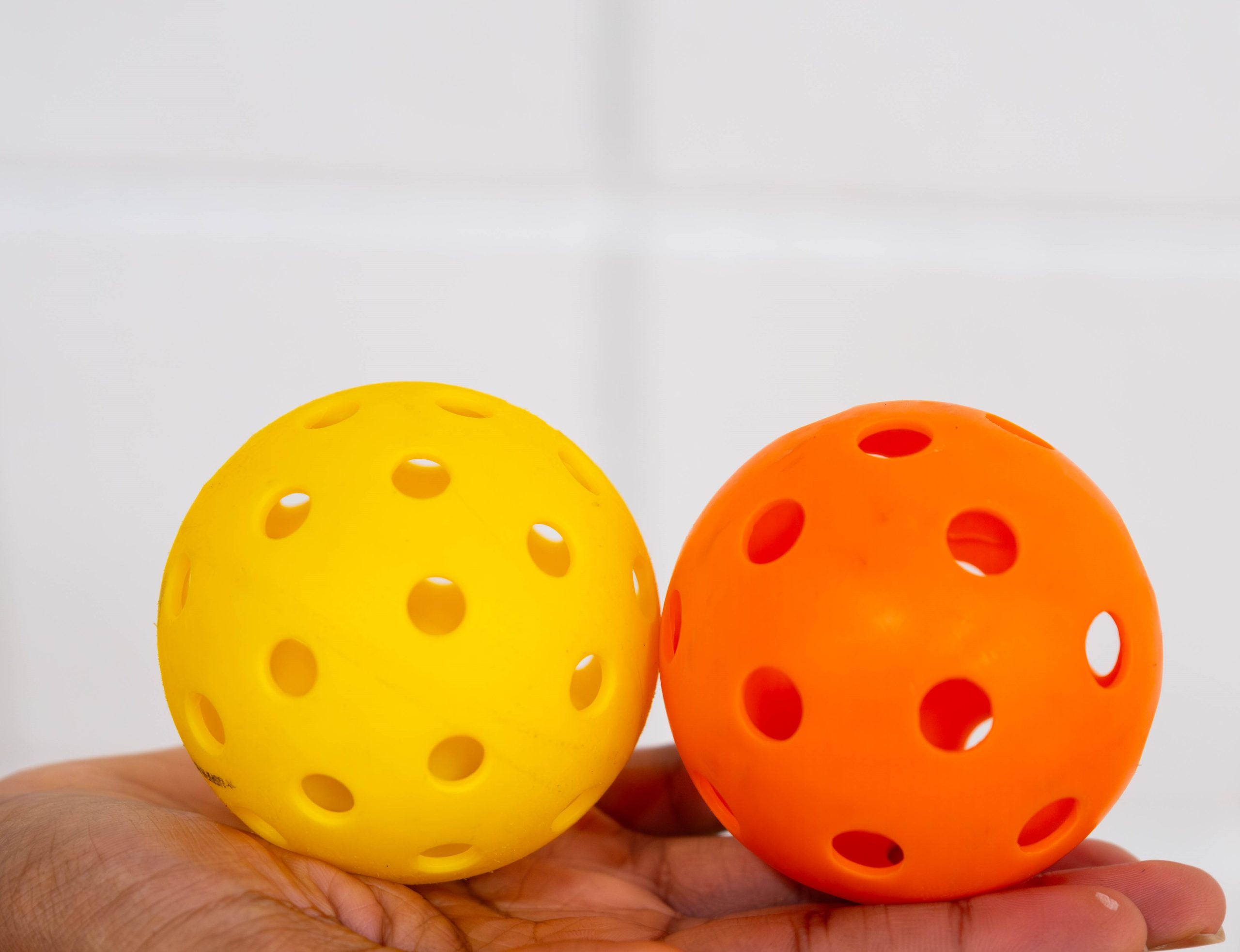 Two balls. Yellow ball on the left is an outdoor ball with more smaller holes, while the orange ball on the right is an indoor ball with larger holes.