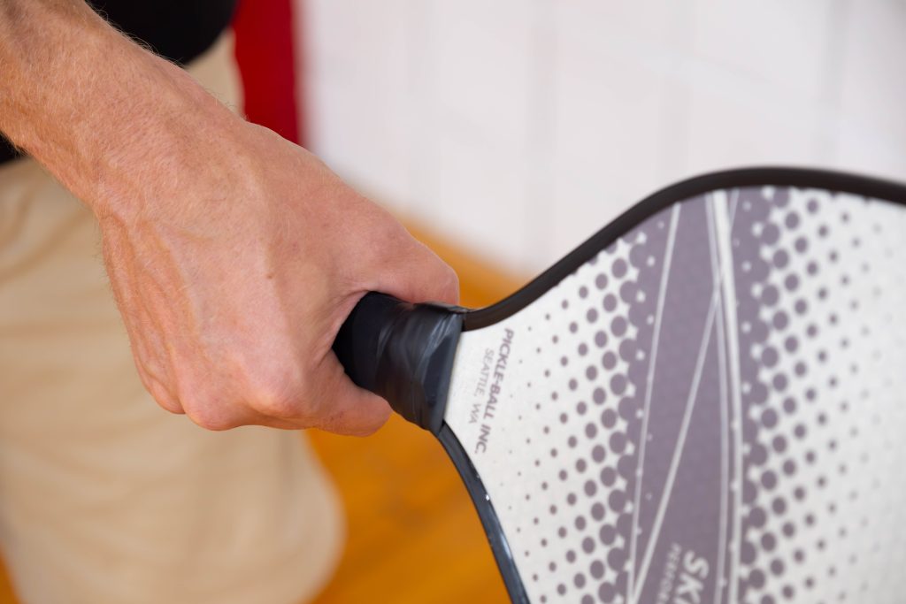 A picture of a hand holding a pickleball paddle.