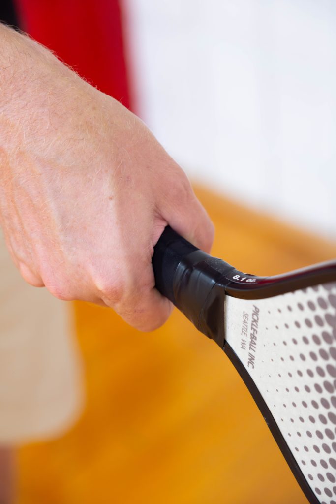 A picture of a hand holding a pickleball paddle.