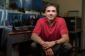 Jonathan Wilker sitting in front of marine animal tank with soft smile.